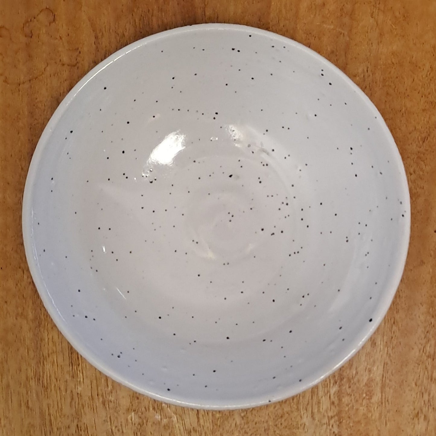 White ceramic bowl with speckled pattern on a wooden surface