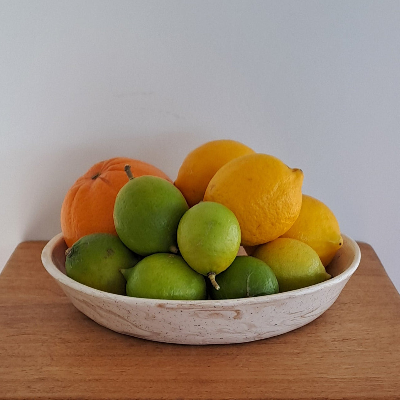 Small bowl with fruits on a wooden stool against a neutral background