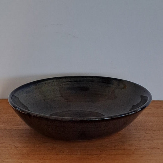 Wooden shelf with a round black bowl on a light gray background