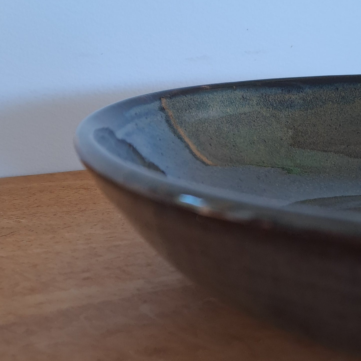 Close-up of a black bowl on a wooden surface with a white wall background