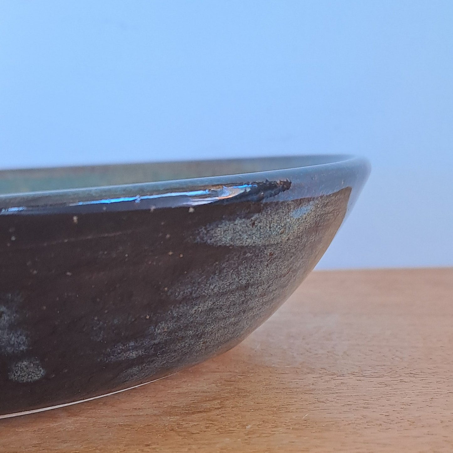 Close-up of a blue black bowl on a wooden surface with a light blue background