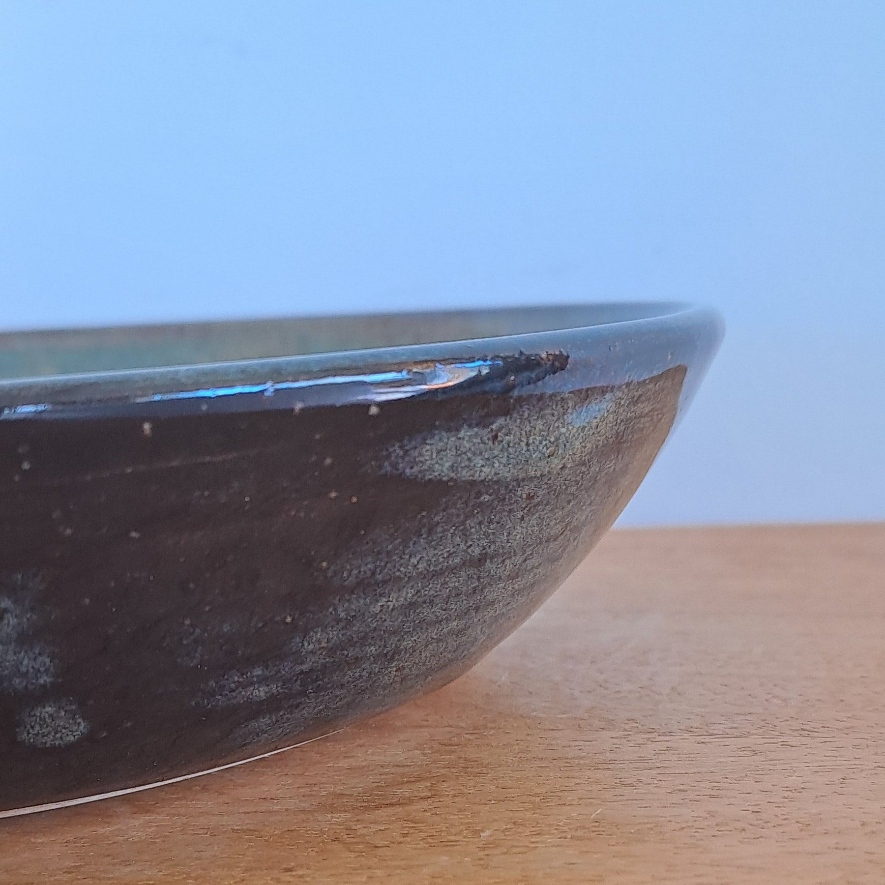 Close-up of a blue black bowl on a wooden surface with a light blue background