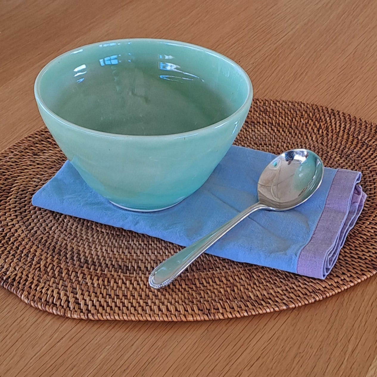 Light green mug with spoon on a woven placemat on a wooden table