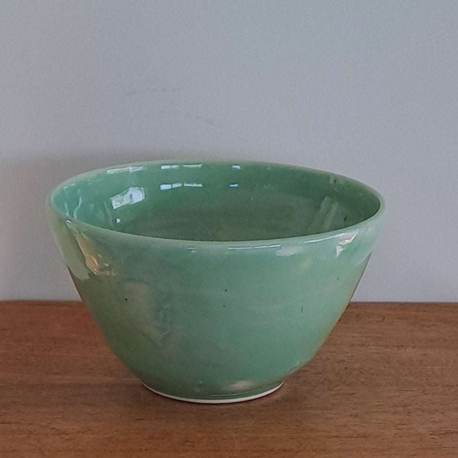 Green bowl on a wooden stool against a light-colored wall.