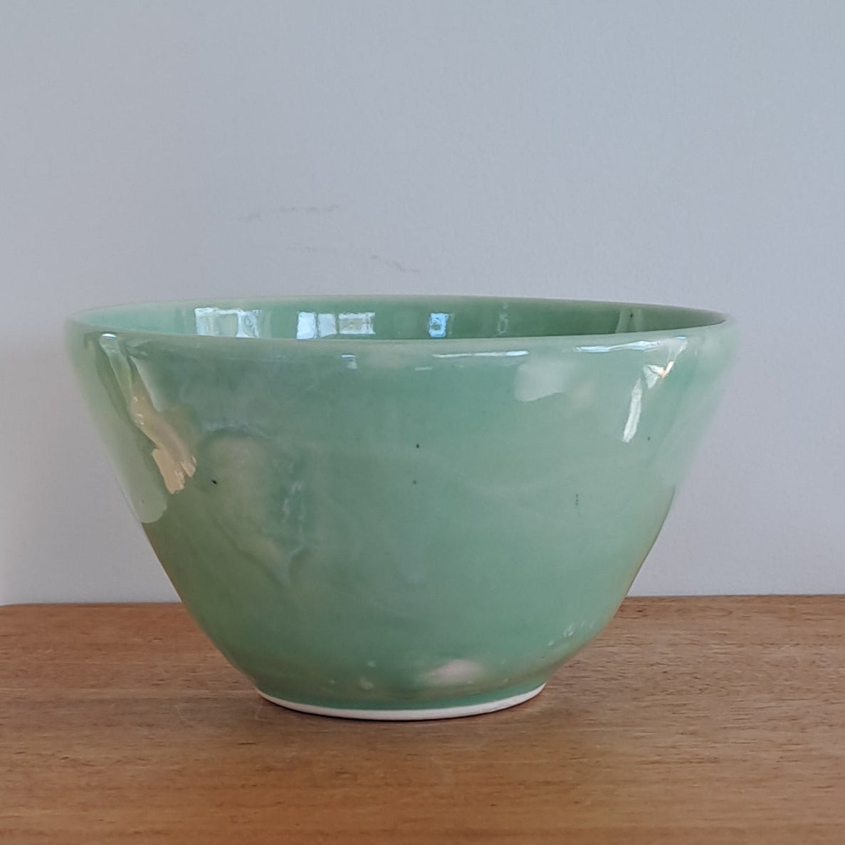 Green bowl on a wooden stool against a light-colored wall.