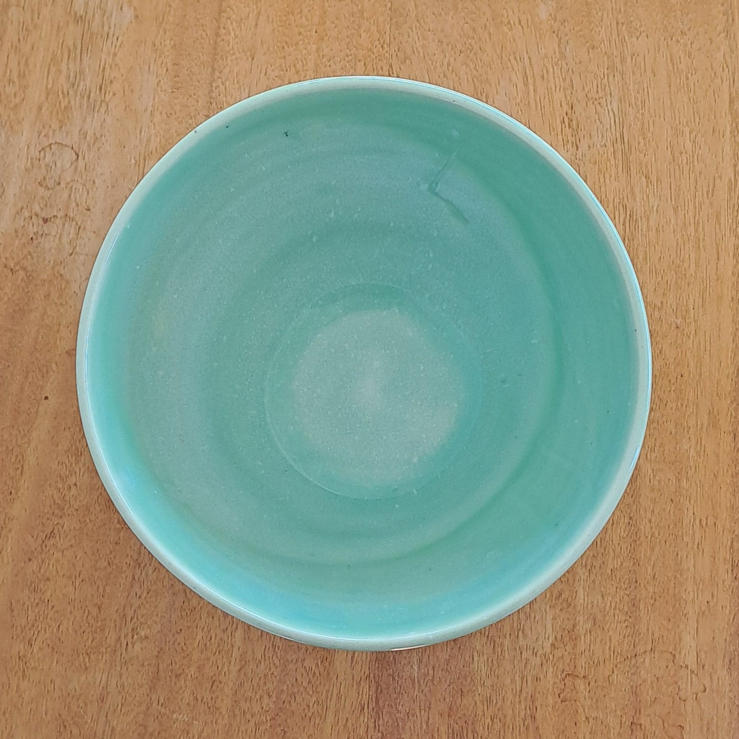 Green bowl on a wooden stool against a light-colored wall.