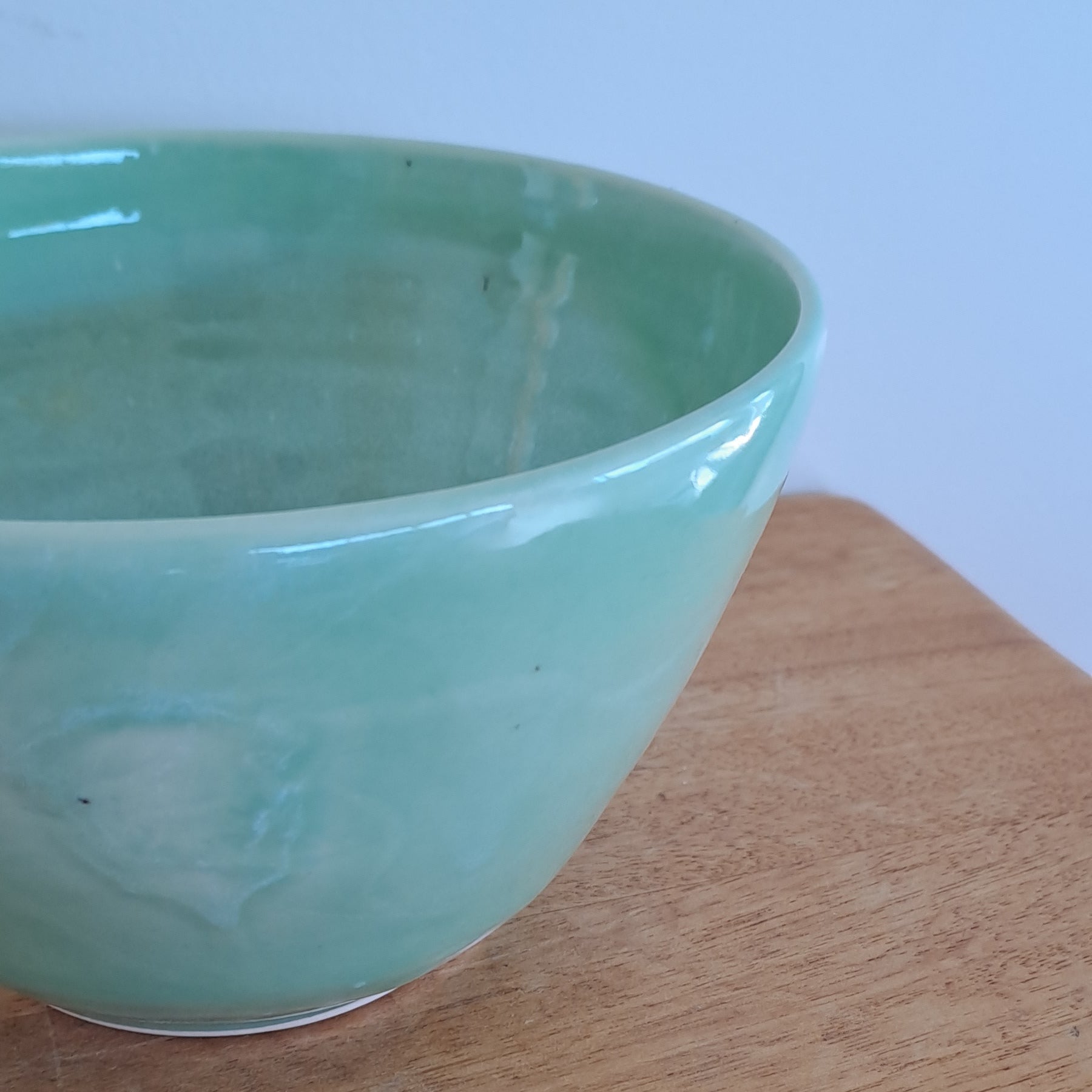 Green ceramic bowl on a wooden surface with a light blue background