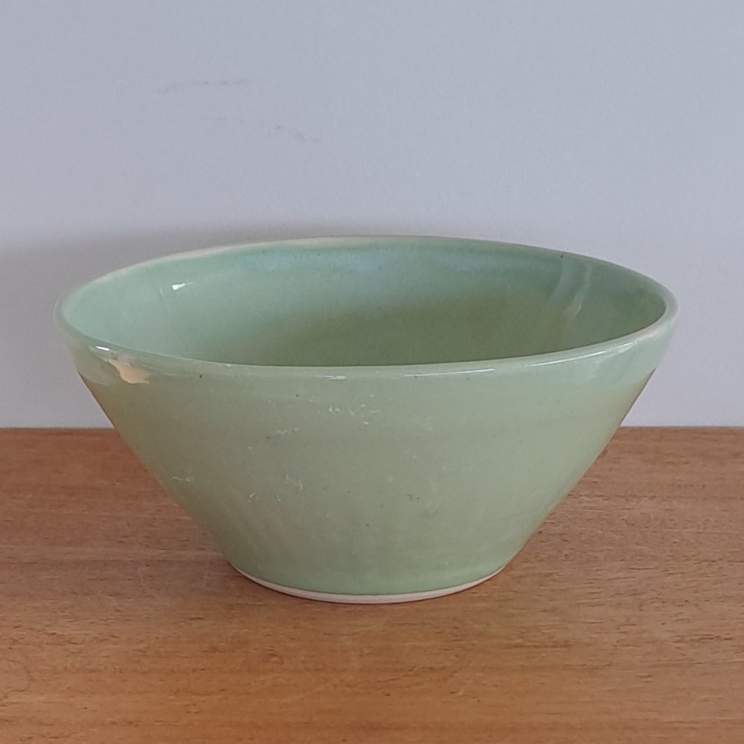 Green bowl on a wooden stool against a light-colored wall.