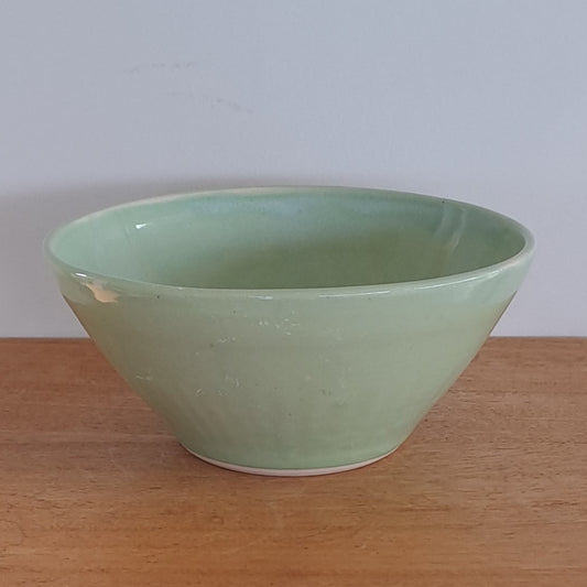 Green bowl on a wooden stool against a light-colored wall.