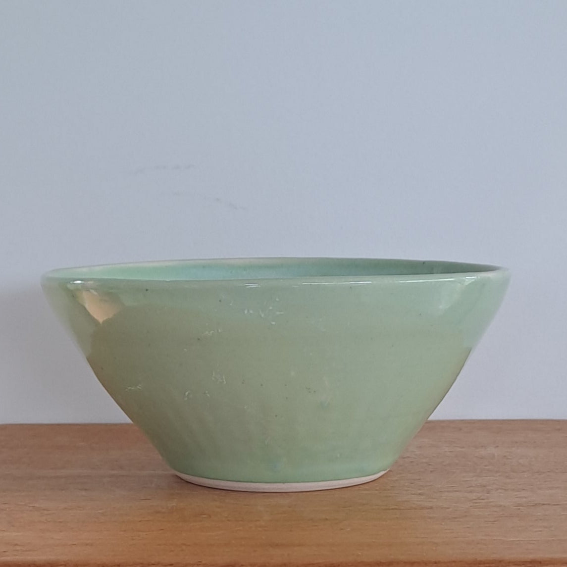 Green bowl on a wooden stool against a light-colored wall.