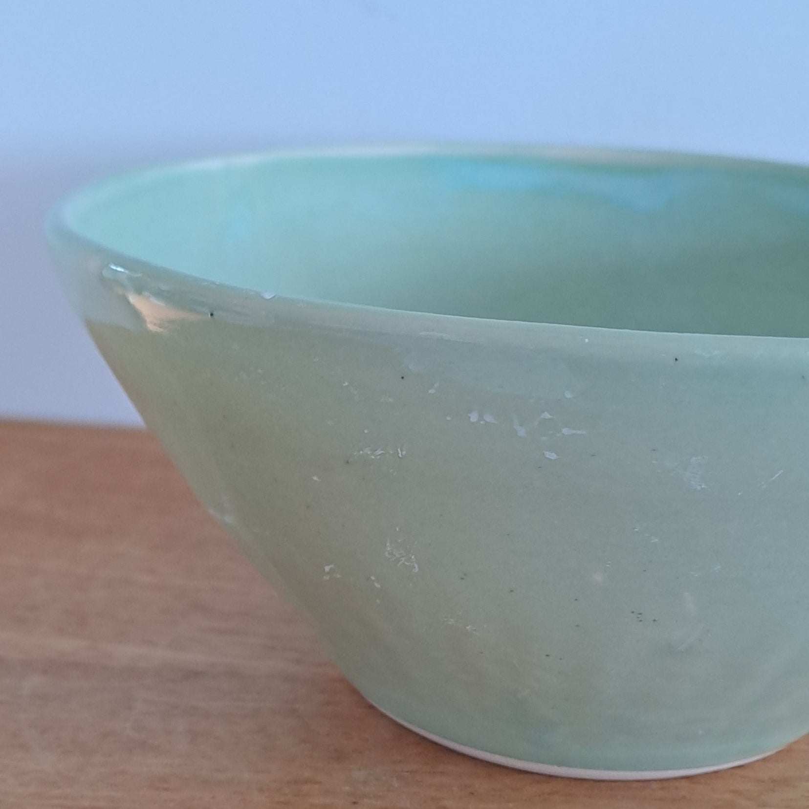 Green bowl on a wooden stool against a light-colored wall.