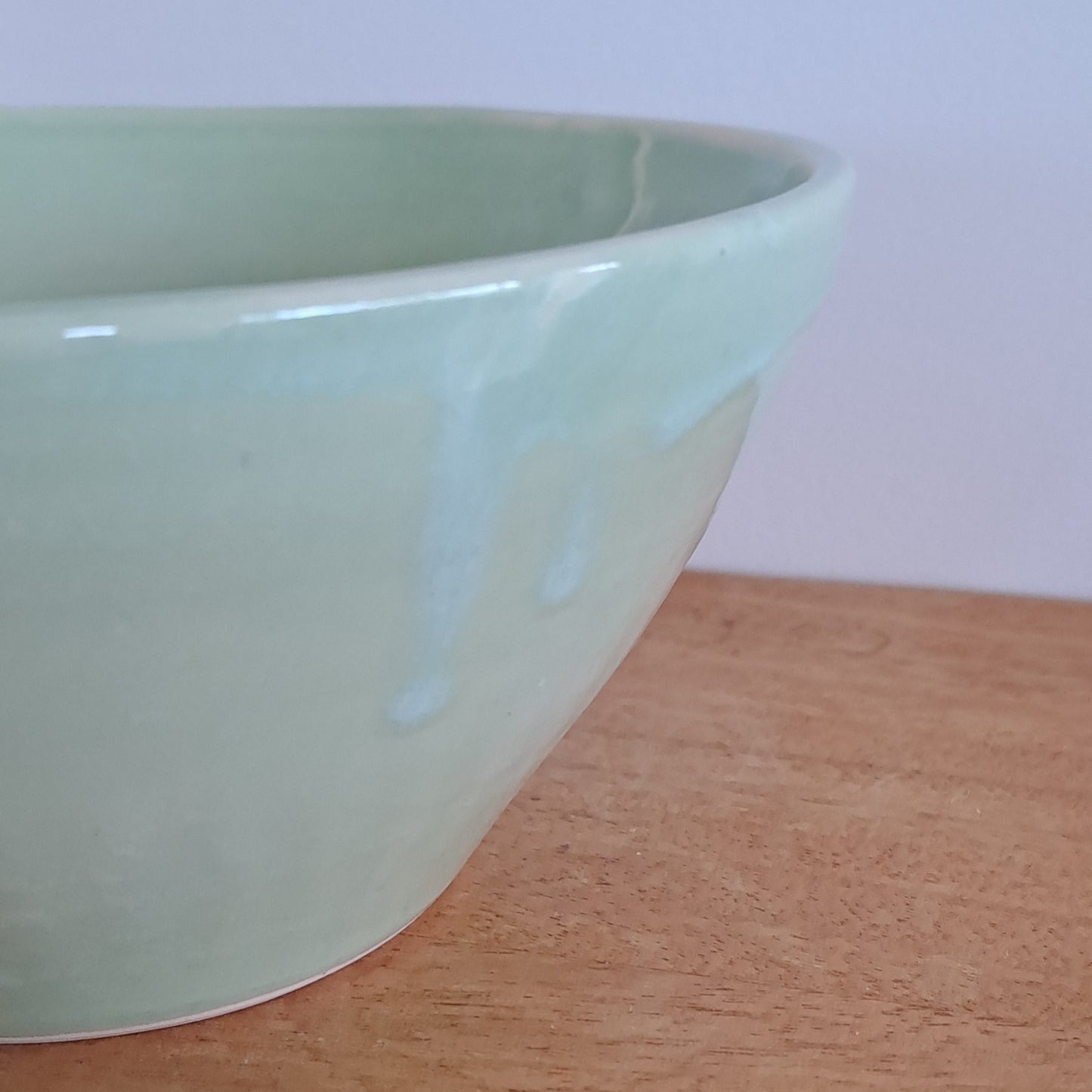 Light green ceramic bowl on a wooden surface with a white background