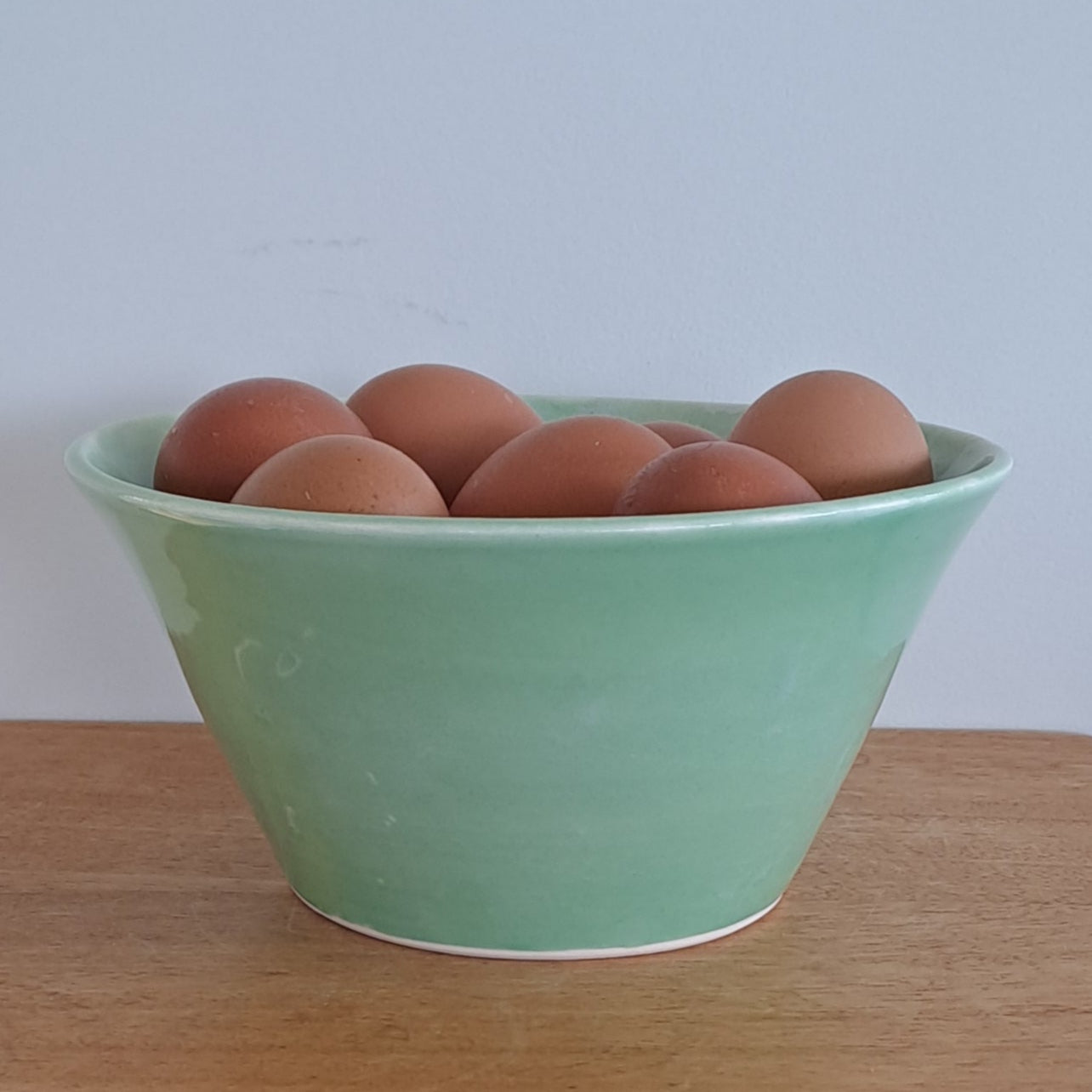 Green bowl with eggs on a wooden stool against a textured wall.