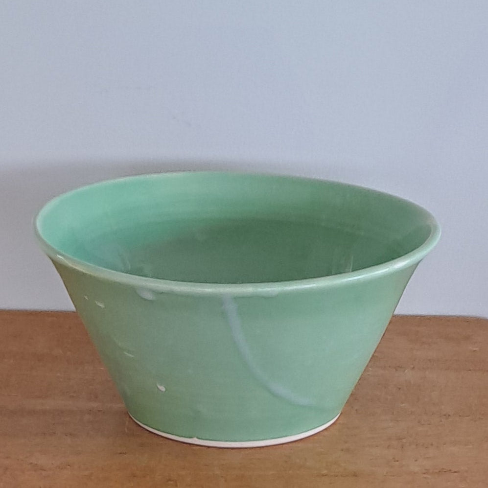 Green bowl on a wooden stool against a textured wall.
