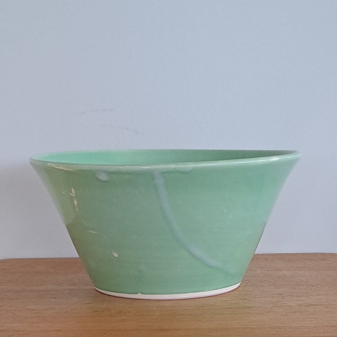 Green bowl on a wooden stool against a textured wall.