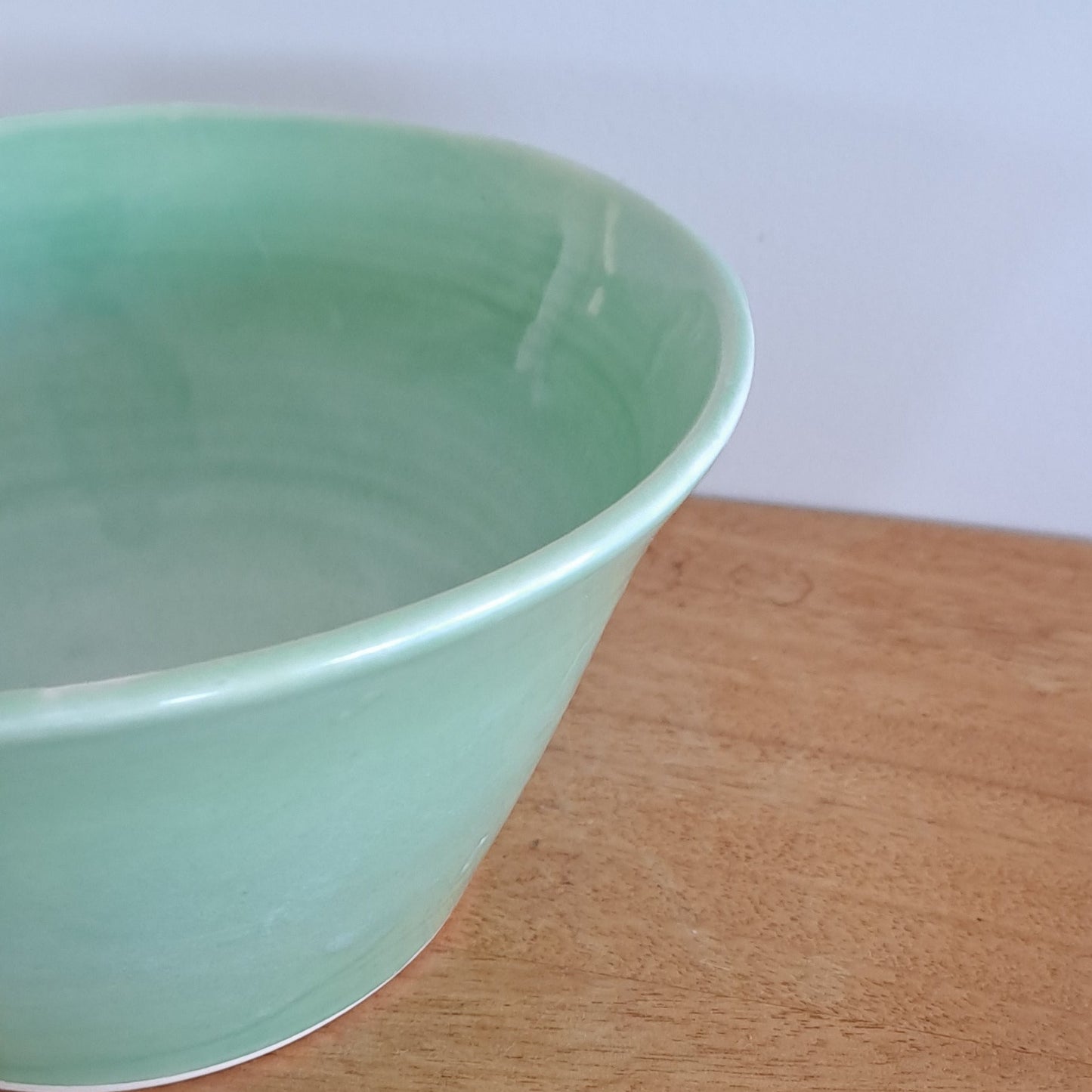 Green ceramic bowl on a wooden surface with a white background