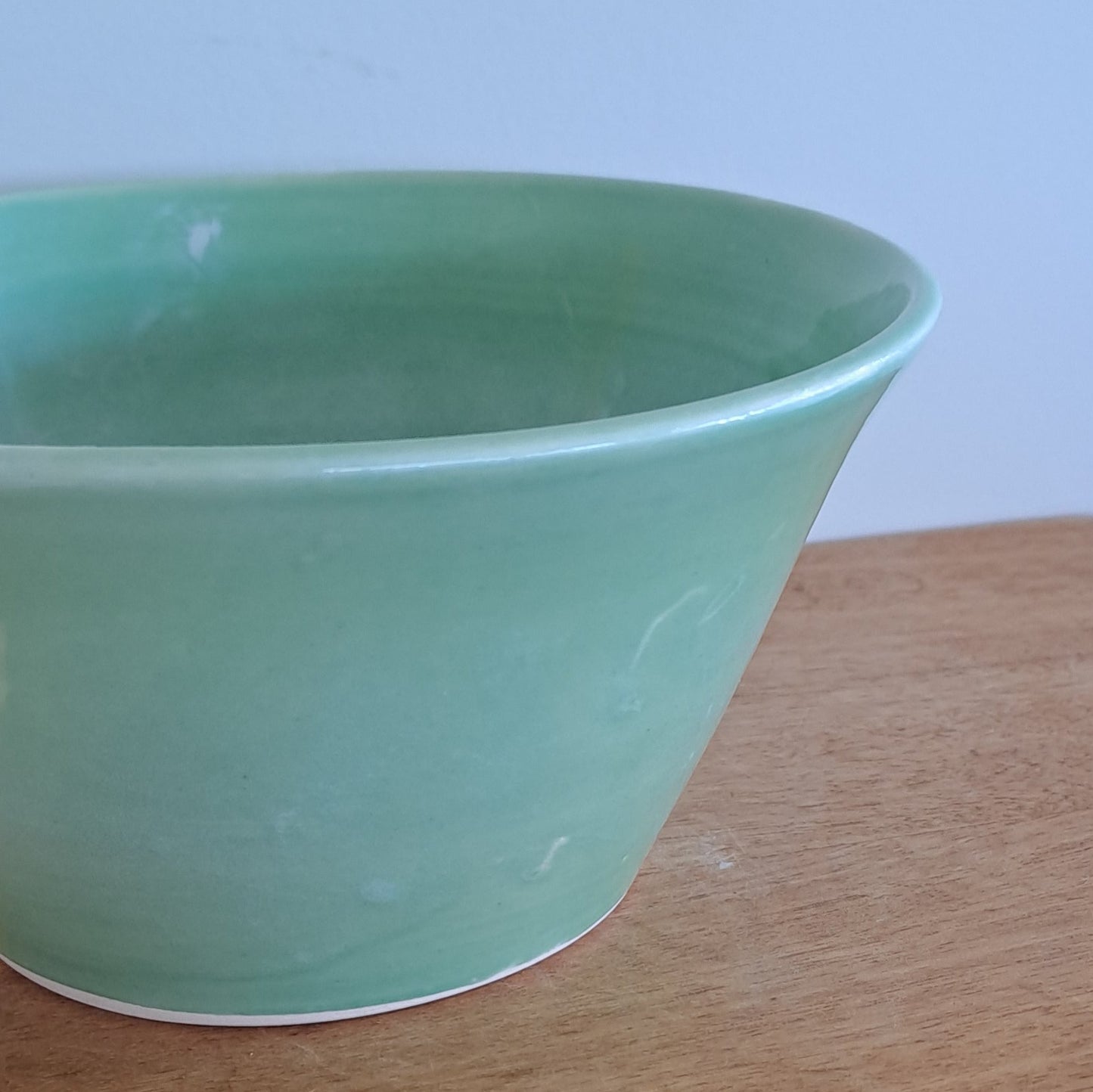 Green bowl on a wooden stool against a textured wall.