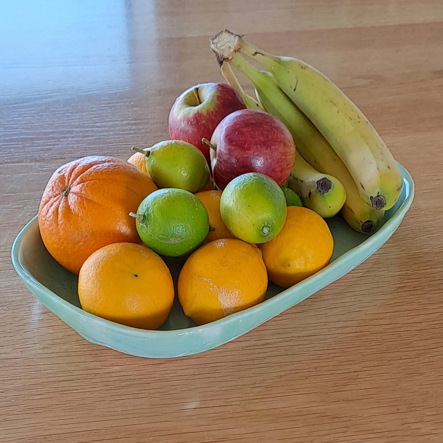 Fruit bowl with bananas, apples, and oranges on a wooden table