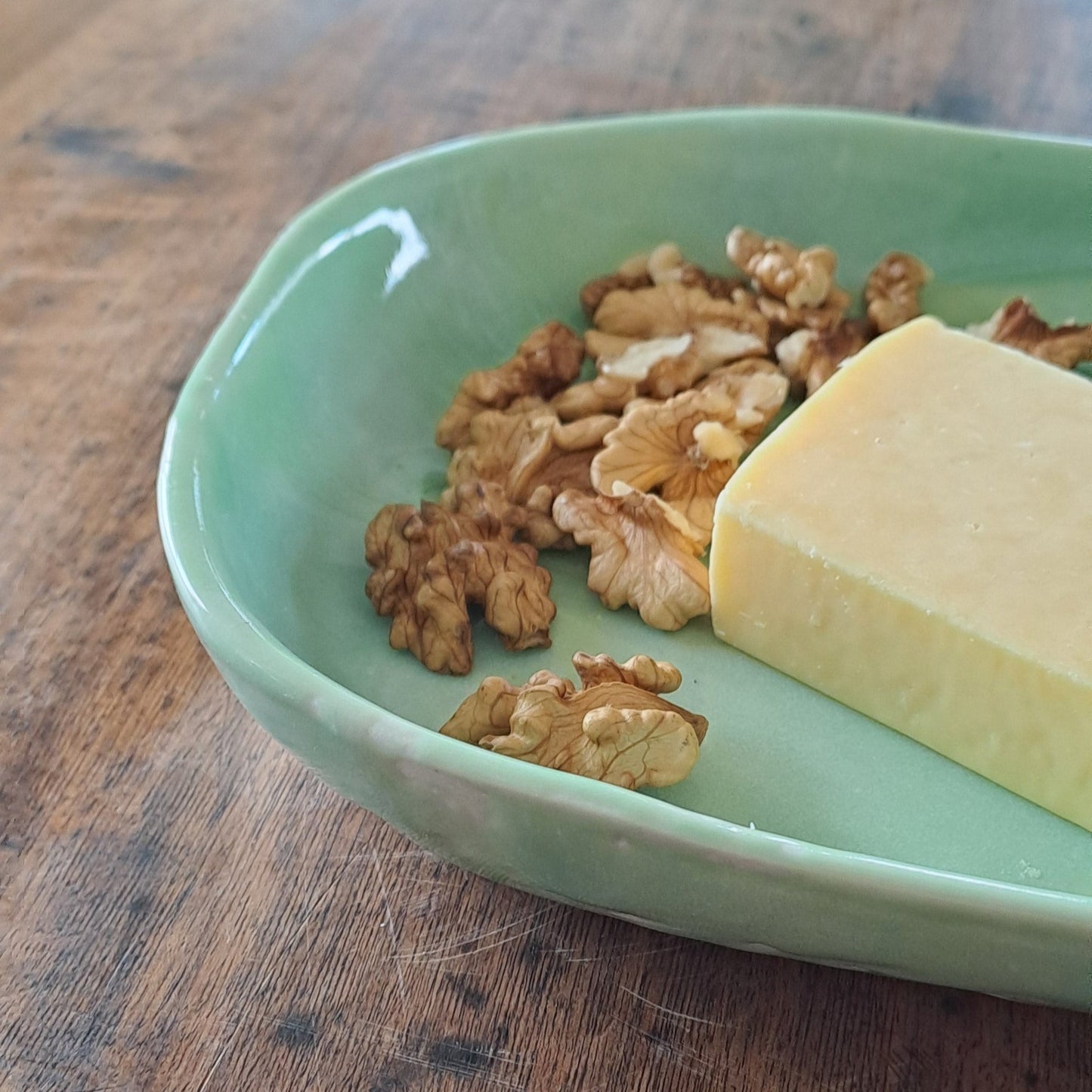 Green ceramic platter with cheese and walnuts on a wooden surface with a white background