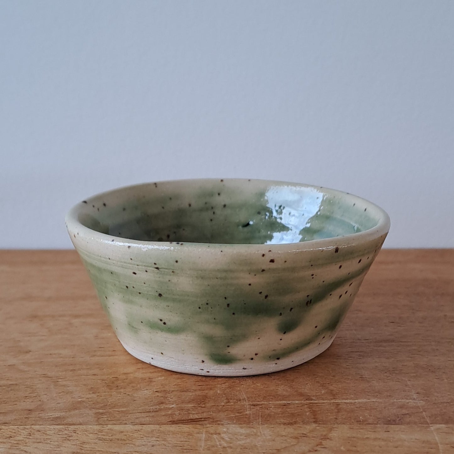 Small ceramic bowl with green speckles on a wooden surface