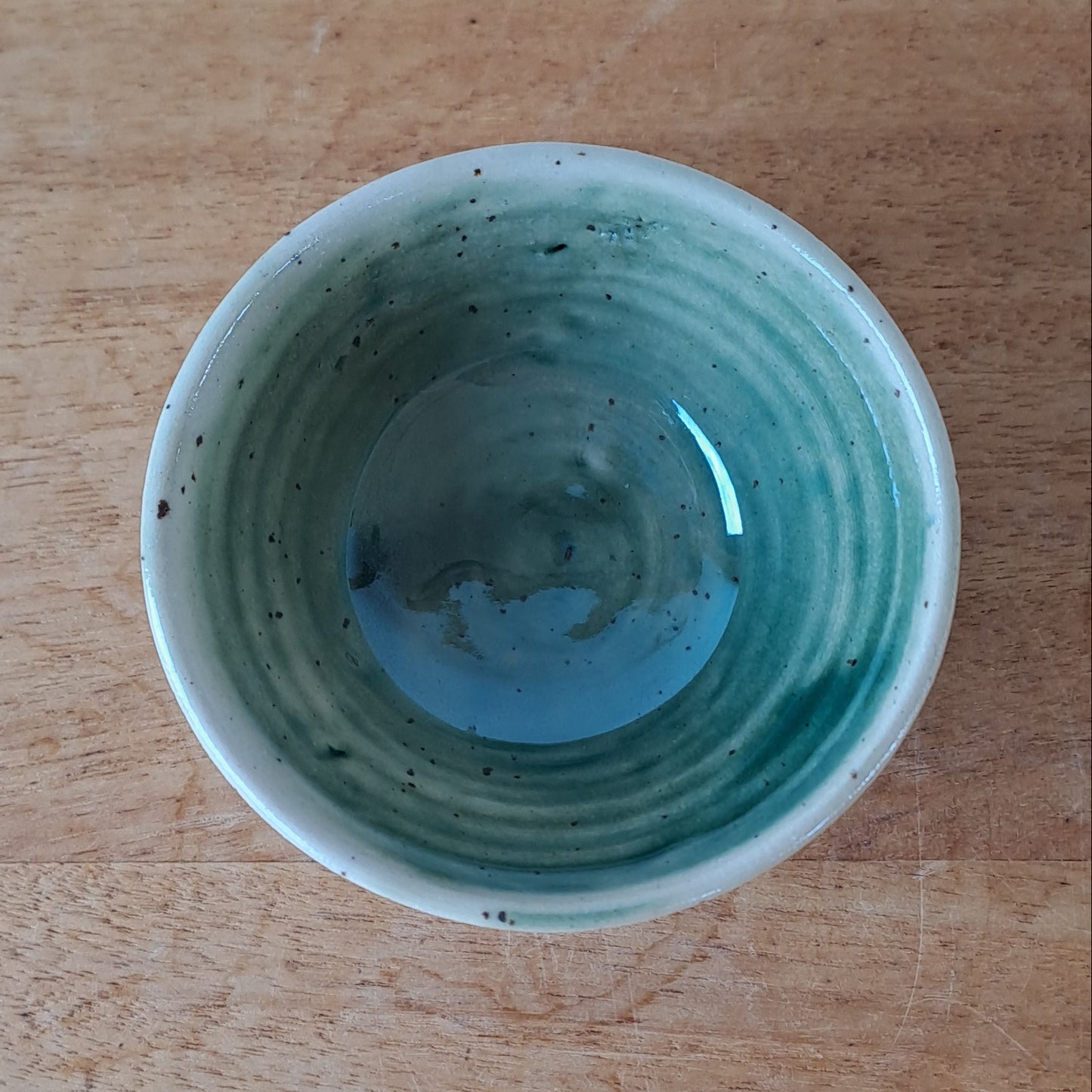 Small ceramic bowl with green speckles on a wooden surface