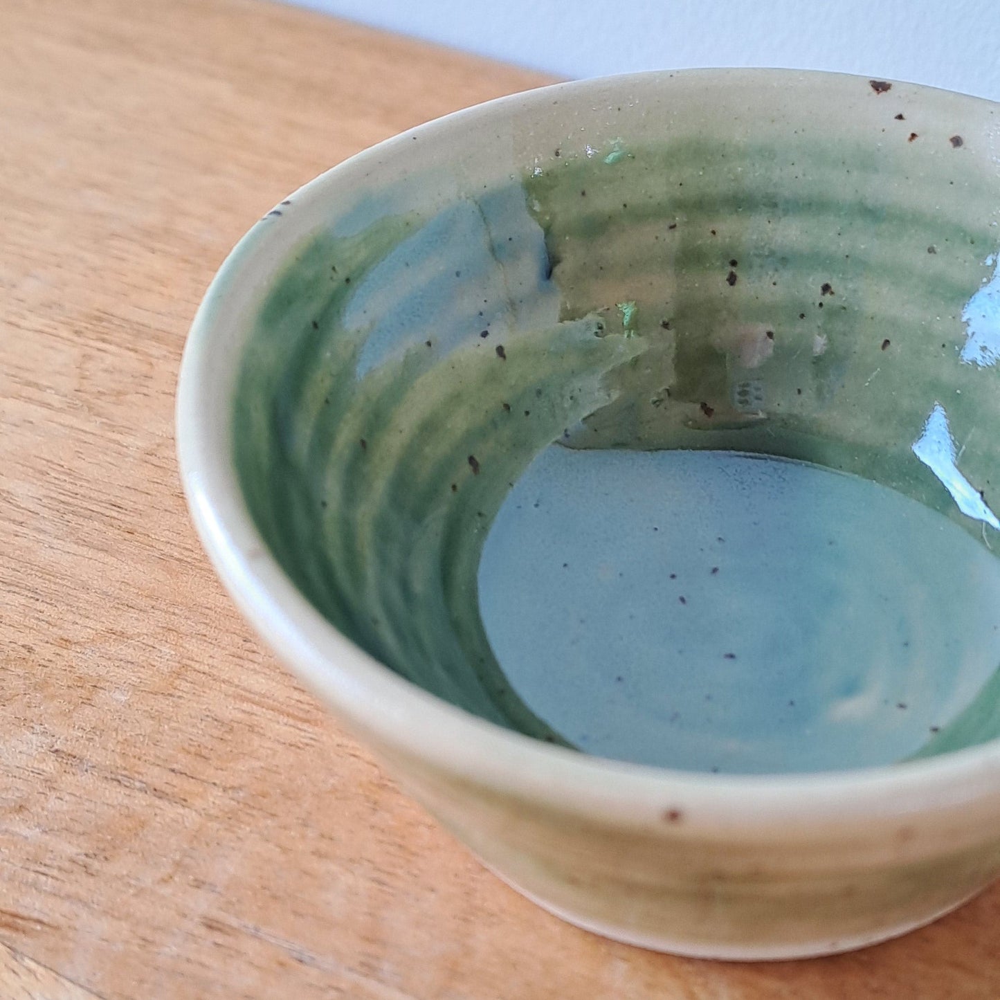 Small ceramic bowl with green and speckles on a wooden surface