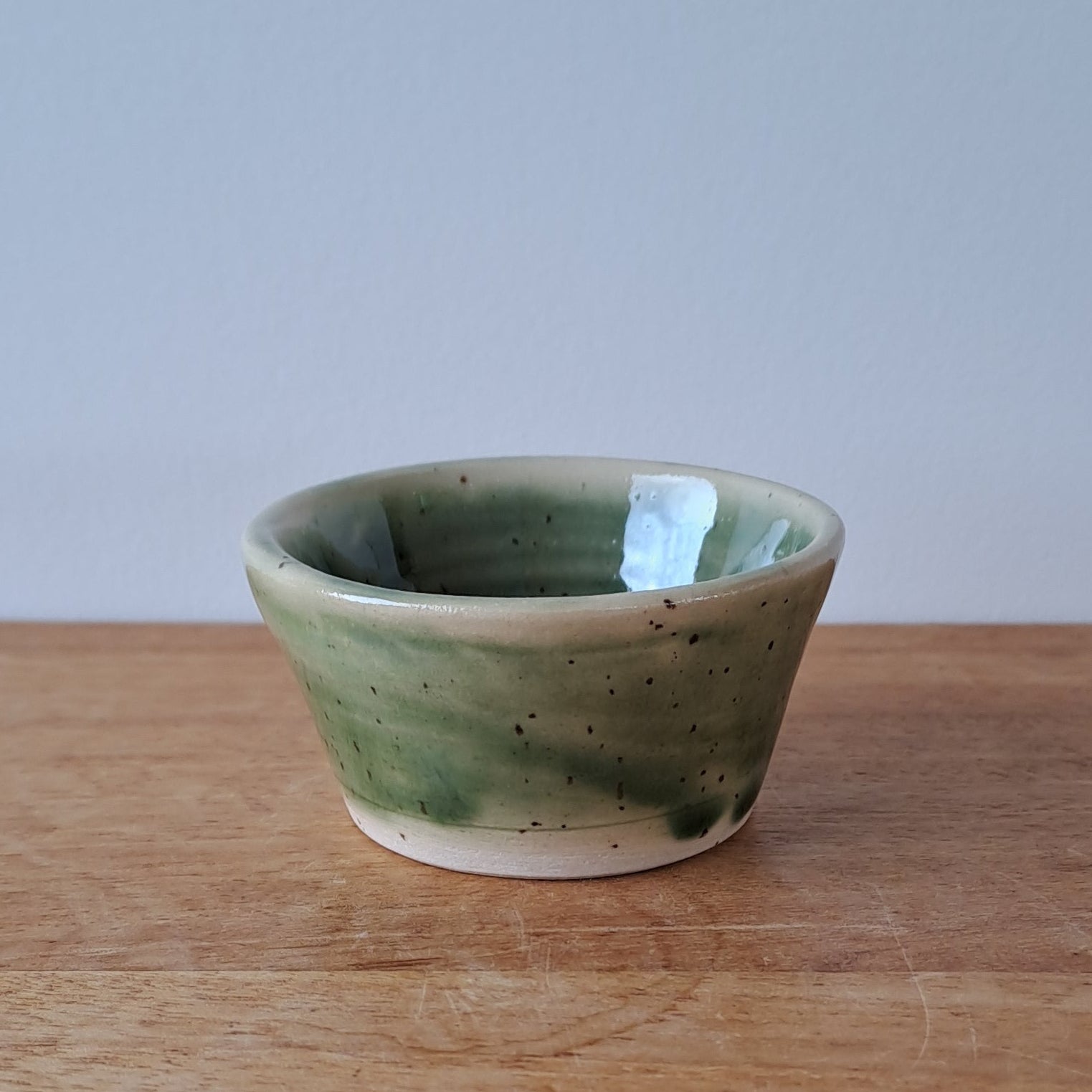 Small ceramic bowl with green and speckles on a wooden surface