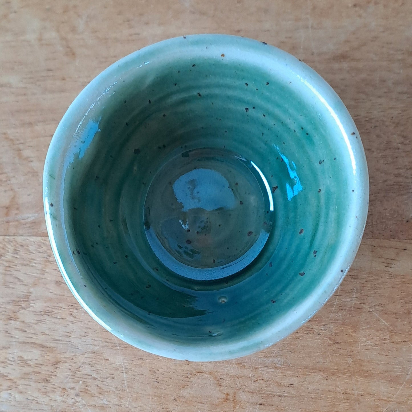 Small ceramic bowl with green and speckles on a wooden surface