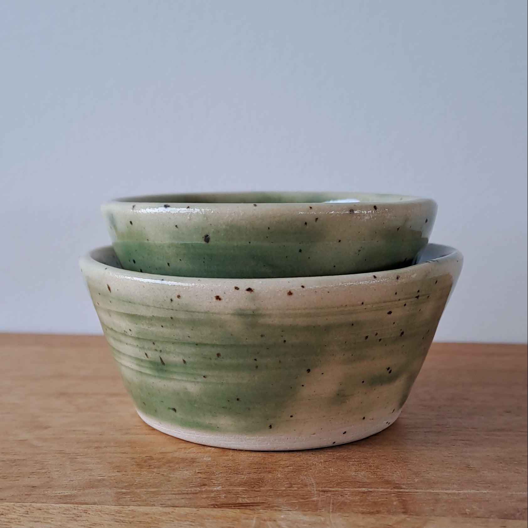 Small ceramic bowls with green and speckles on a wooden surface