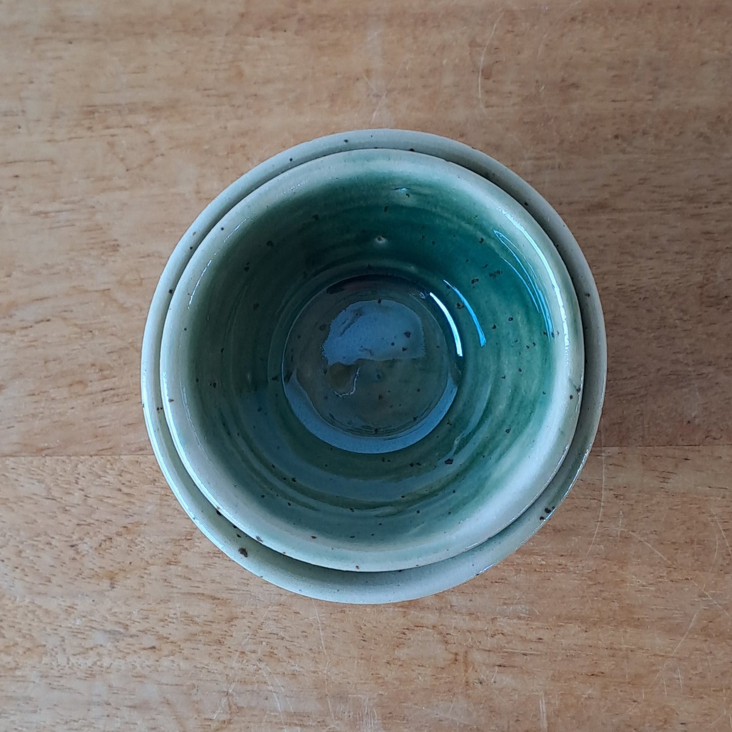 Small ceramic bowls with green and speckles on a wooden surface
