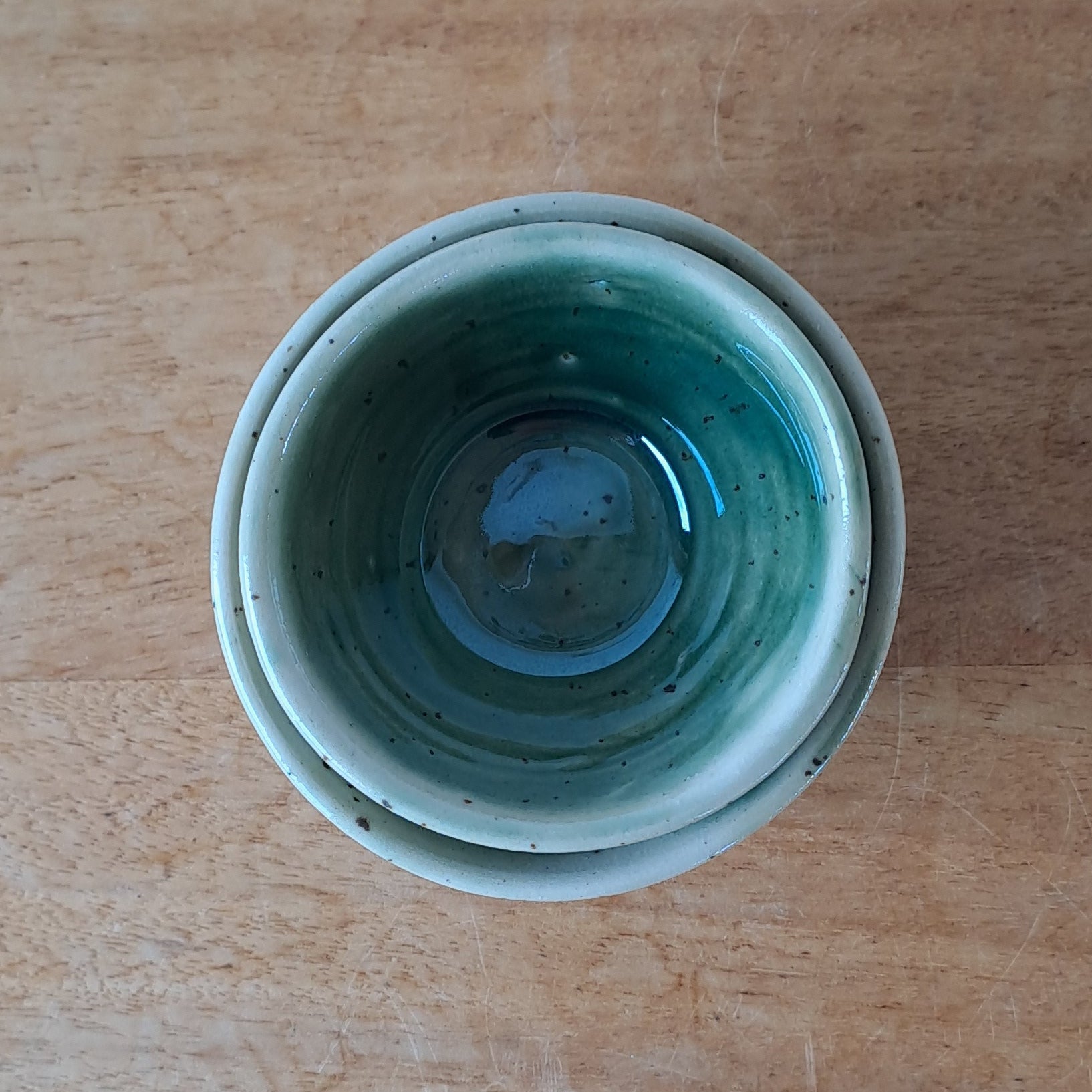 Small ceramic bowls with green and speckles on a wooden surface