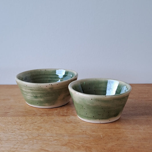 Small ceramic bowls with green and speckles on a wooden surface