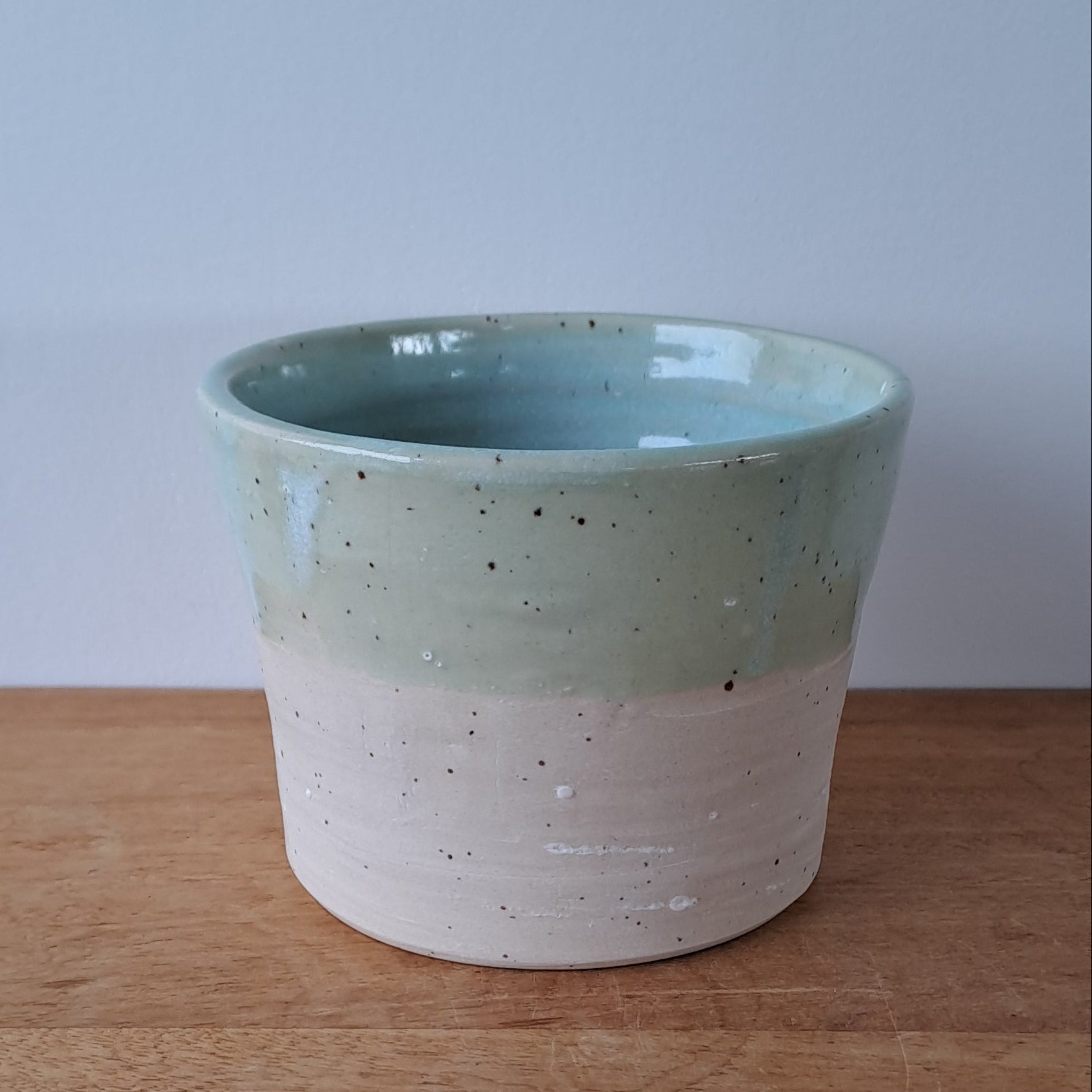 Ceramic speckled planter with blue green glaze on a wooden surface with a white background