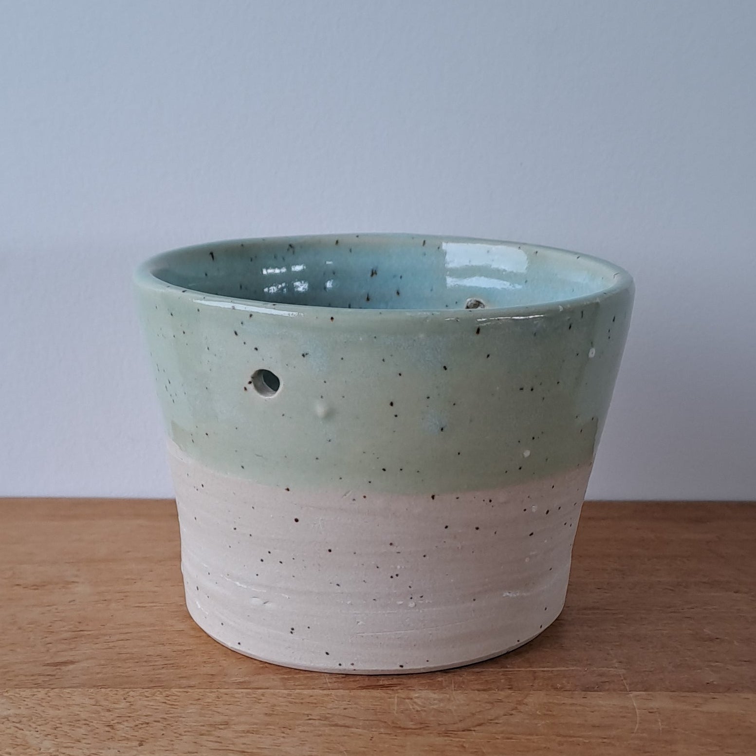 Ceramic speckled planter with blue green glaze on a wooden surface with a white background