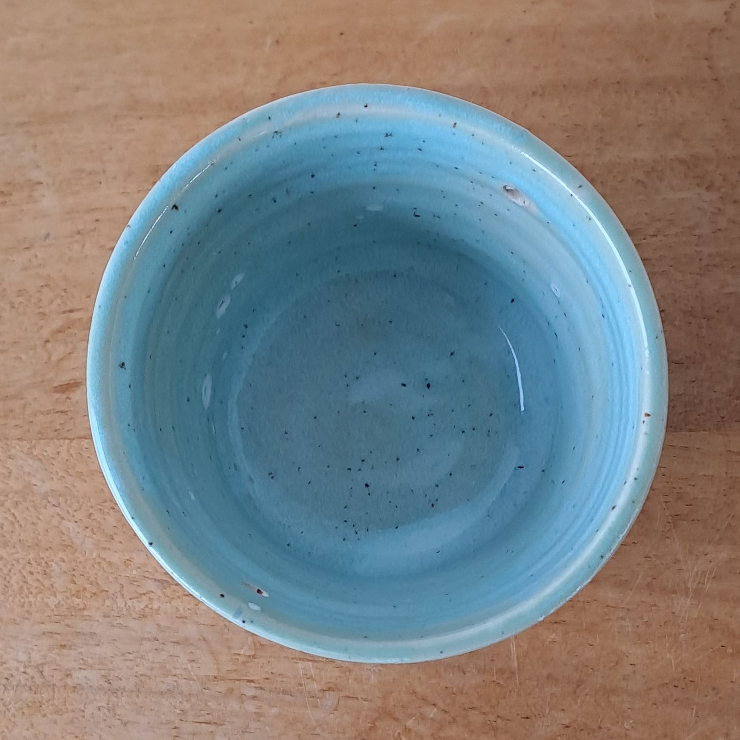 Ceramic speckled planter with blue green glaze on a wooden surface with a white background