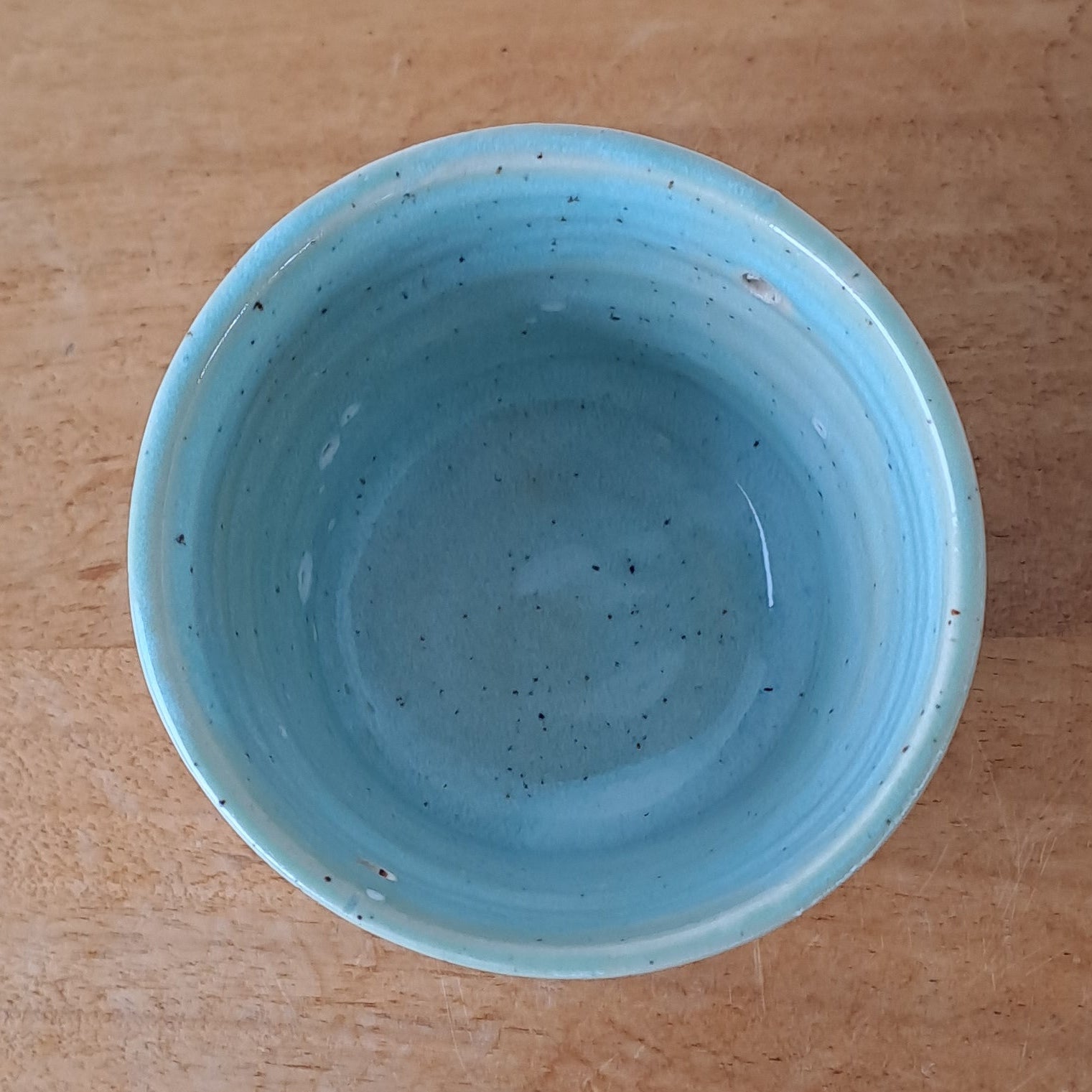 Ceramic speckled planter with blue green glaze on a wooden surface with a white background