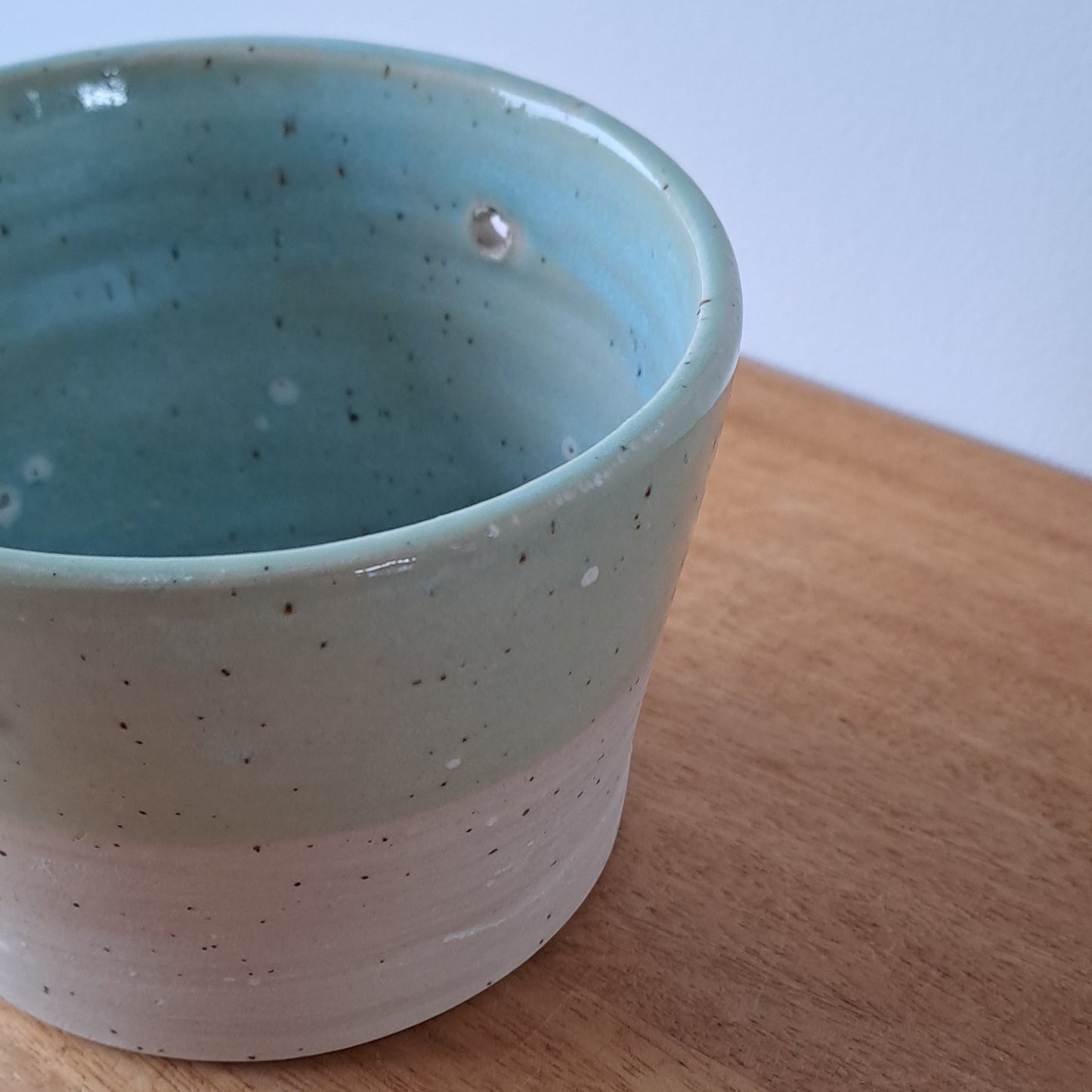Ceramic speckled planter with blue green glaze on a wooden surface with a white background