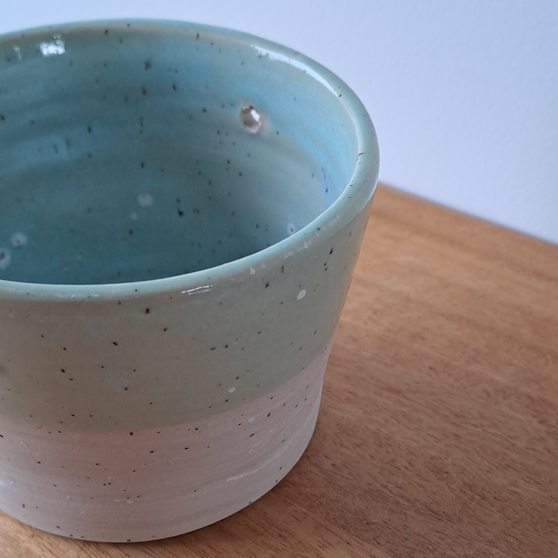Ceramic speckled planter with blue green glaze on a wooden surface with a white background