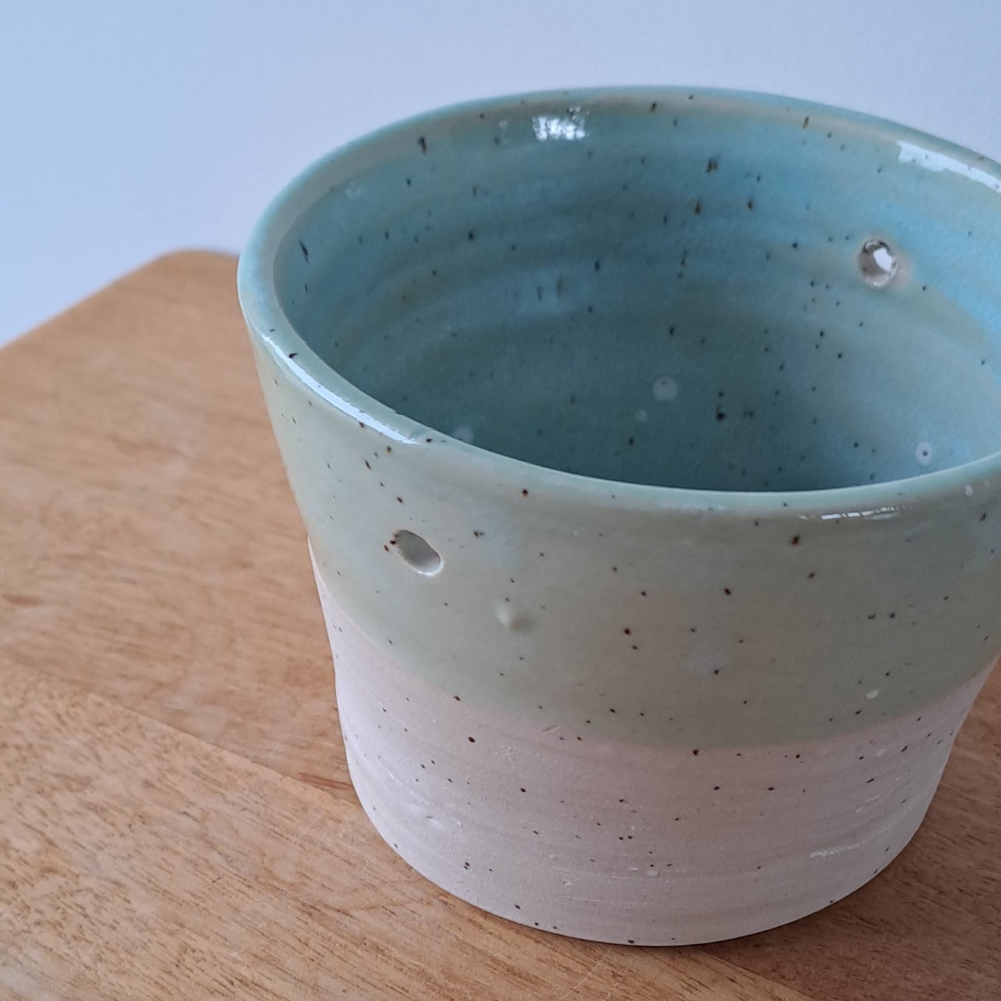 Ceramic speckled planter with blue green glaze on a wooden surface with a white background