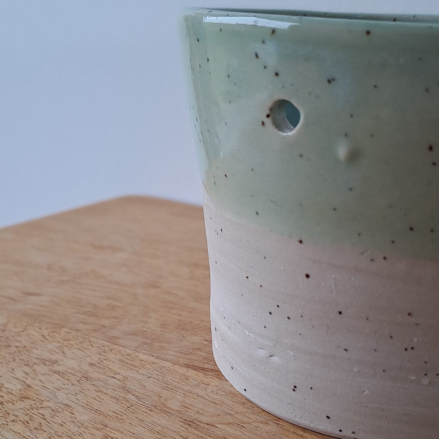Ceramic speckled planter with blue green glaze on a wooden surface with a white background