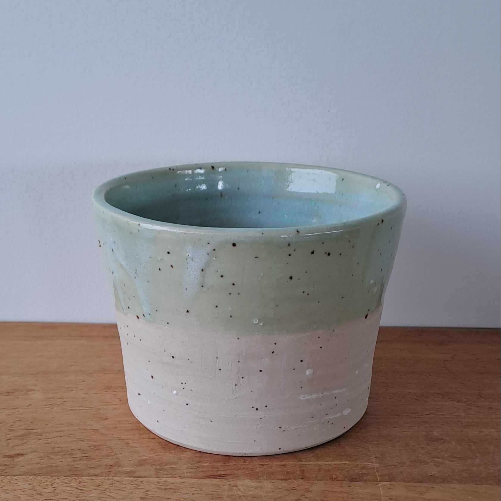 Ceramic speckled planter with blue green glaze on wooden table with light background