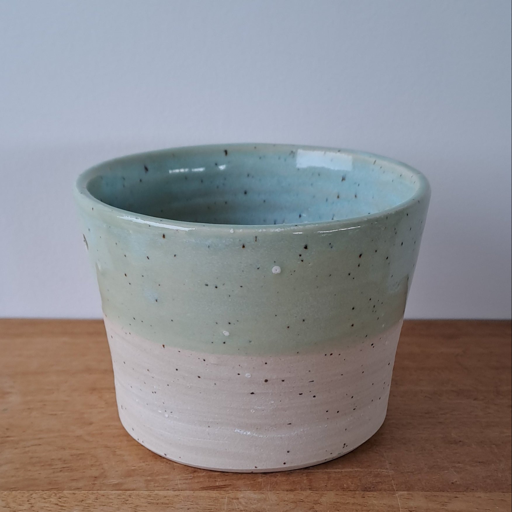 Ceramic speckled planter with blue green glaze on wooden table with light background