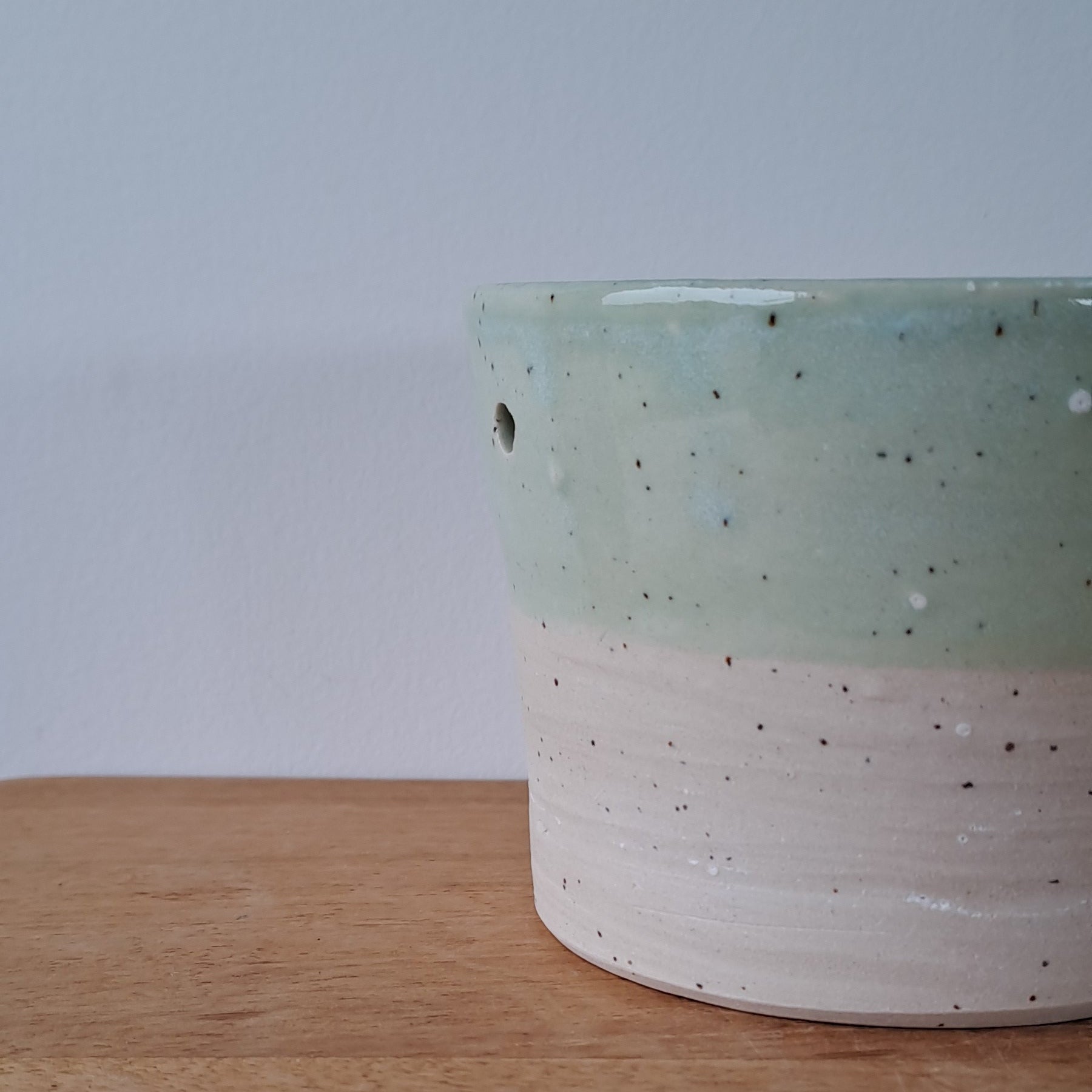 Ceramic speckled planter with blue green glaze on wooden table with light background