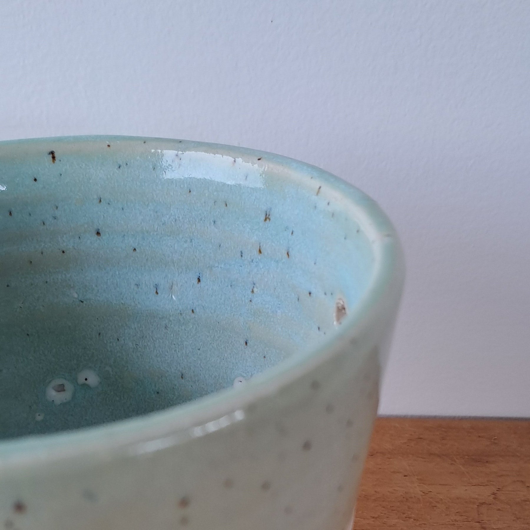 Ceramic speckled planter with blue green glaze on wooden table with light background