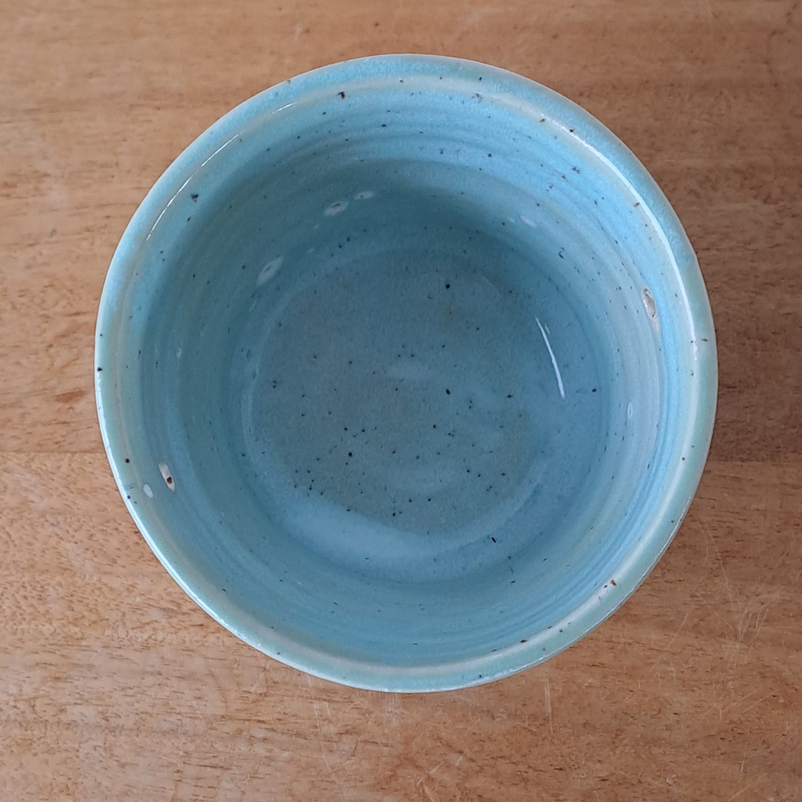 Ceramic speckled planter with blue green glaze on wooden table with light background
