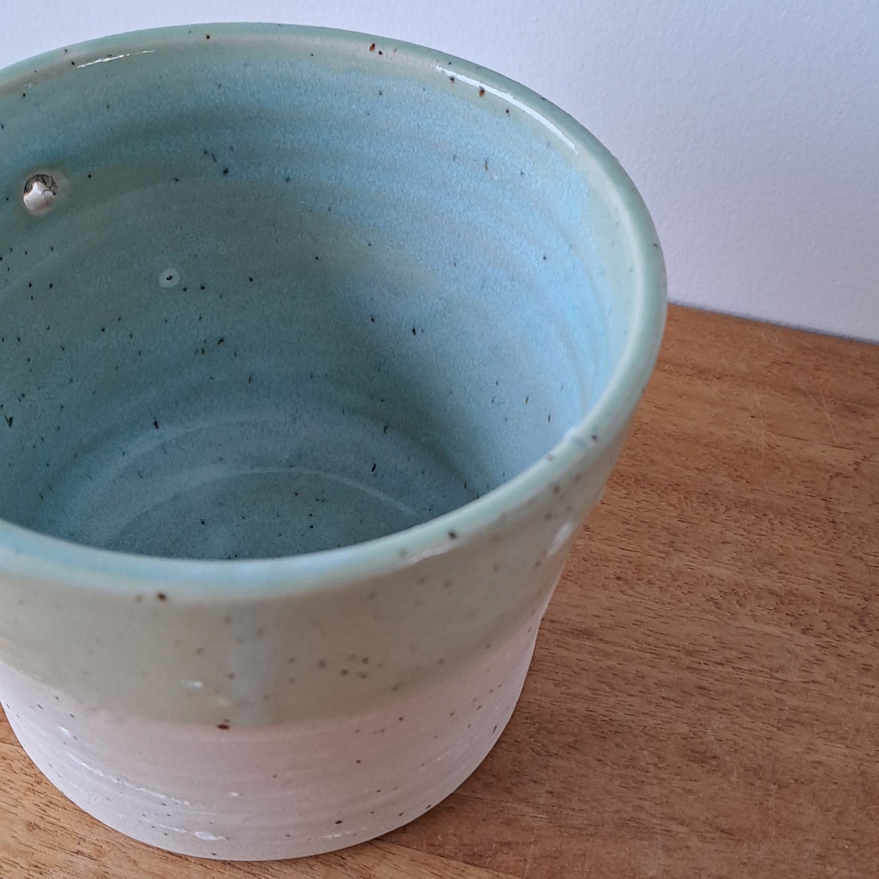 Ceramic speckled planter with blue green glaze on wooden table with light background